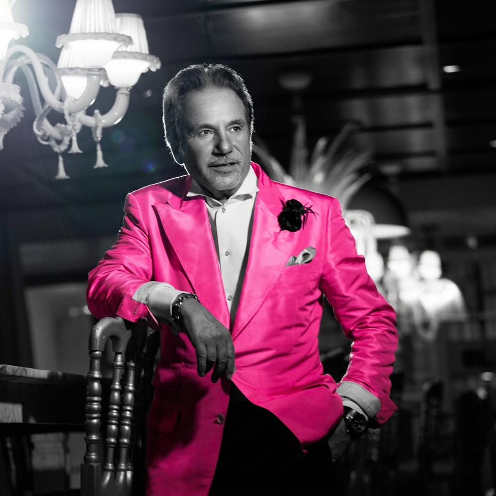 Joe Colangelo in a hot pink jacket against a black and white room